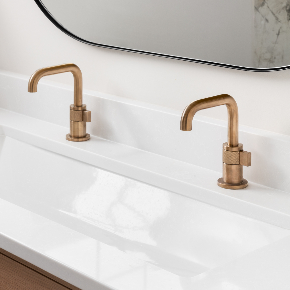 A beautiful bathroom with a white oak cabinet, marble countertop, gold faucets, and a black round mirror.